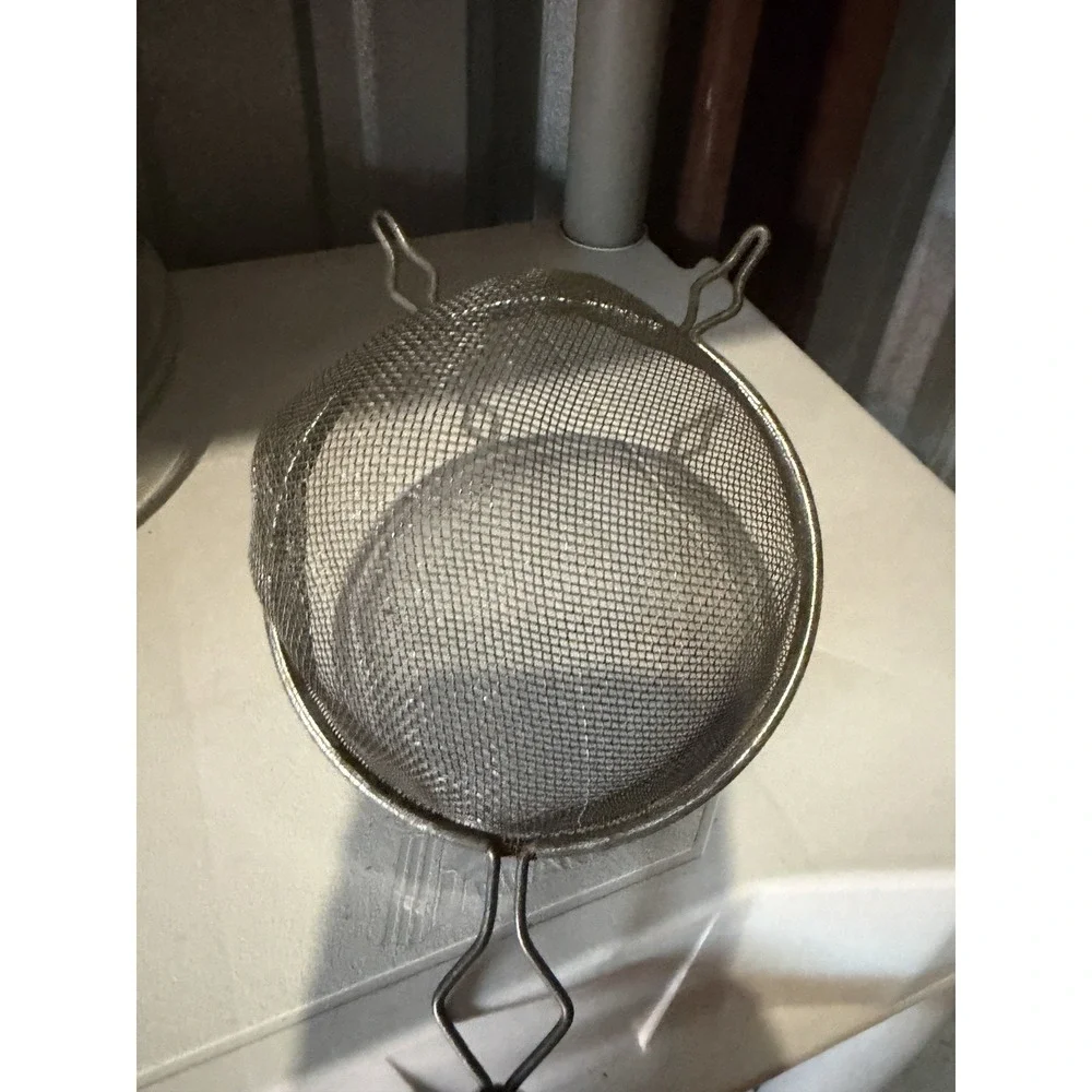The vintage Eckoline hand-held mesh strainer with a yellow and white plastic